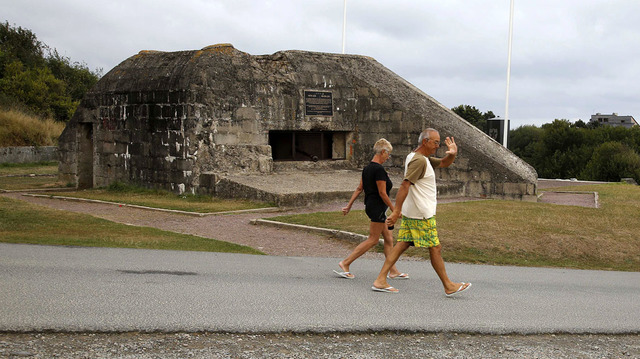 Los turistas caminan delante de un antiguo bunker alemán con vistas a la zona de desembarco del Día D